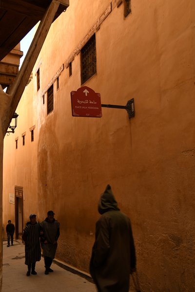 Passanten bij hoge oranje muren in Fez, Marokko