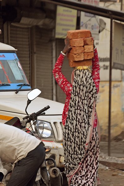 Vrouw die bakstenen op haar hoofd draagt in Delhi (India)